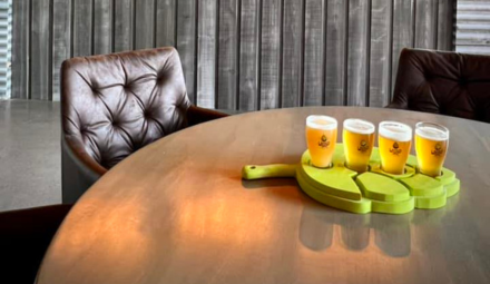 A flight of pale-coloured beers in a hops shaped holder on a bar table.